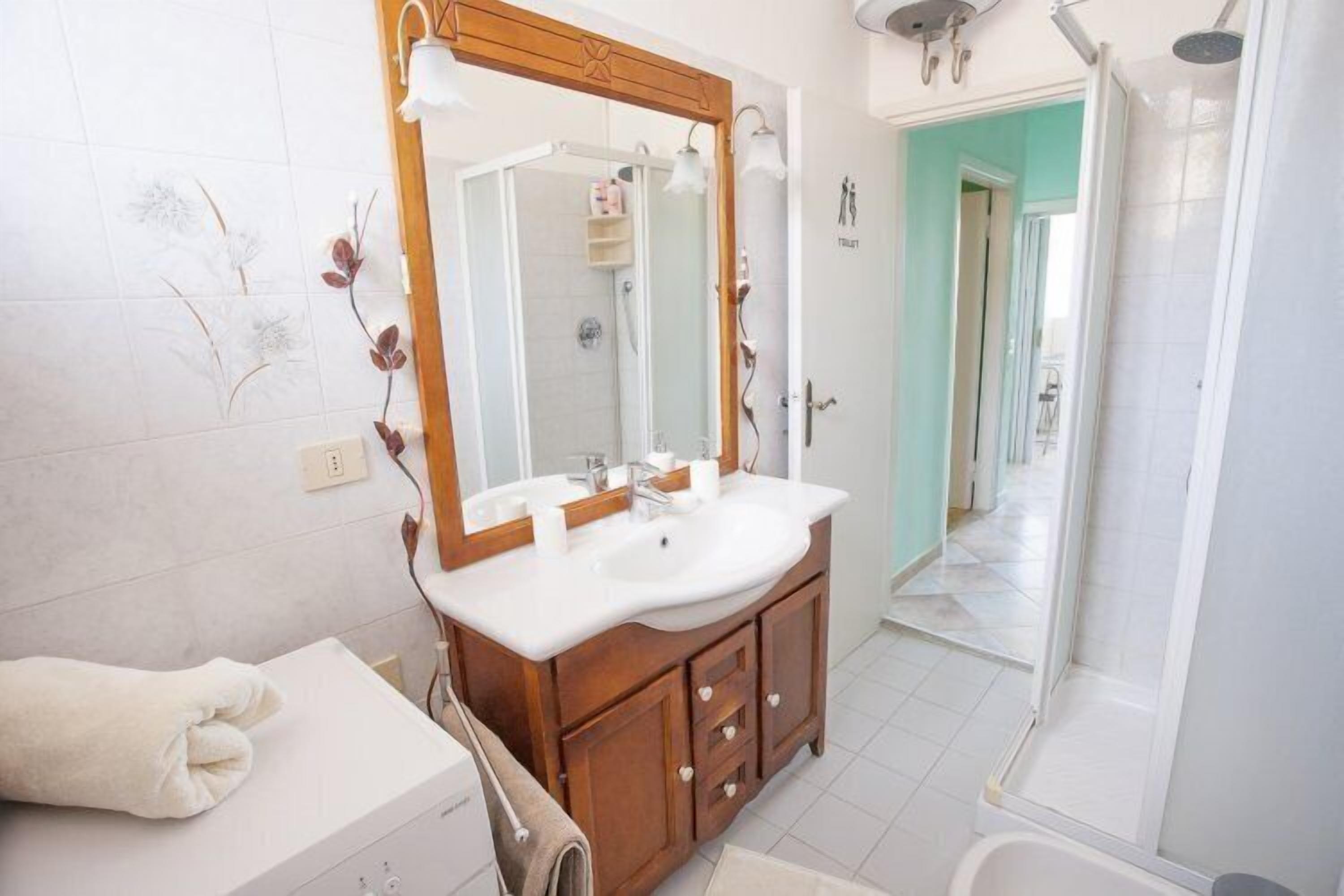 Ein modernes Badezimmer mit einem Holzkosmetikschrank, einem großen Spiegel, einem weißen Waschbecken und einer Duschkabine.