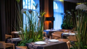 L’intérieur d’un restaurant, avec des tables dressées pour le service, entouré de grandes plantes et d’éléments décoratifs.