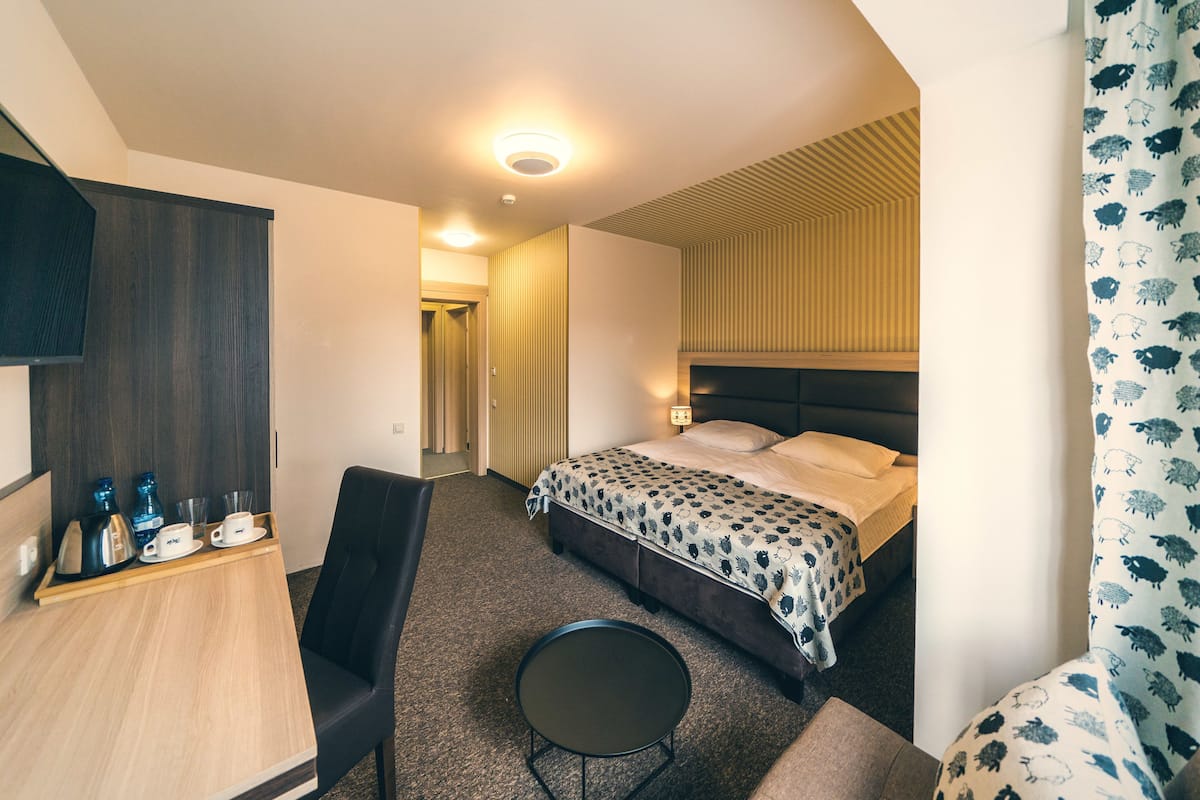 Een hotelkamer met een bed, een bureau met een dienblad en spullen, een stoel en een klein rond tafeltje.