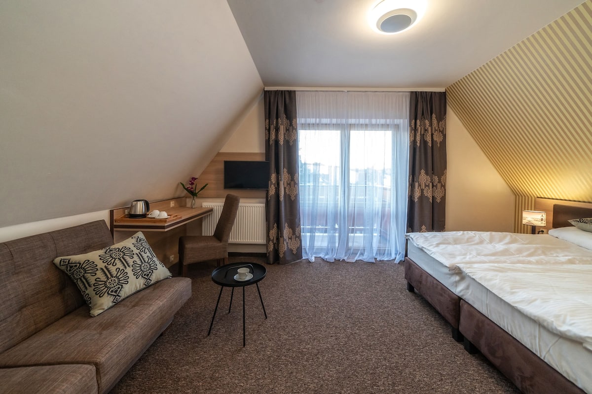 Een hotelkamer met een bed, een bank, een klein tafeltje, een televisie en een raam met gordijnen.