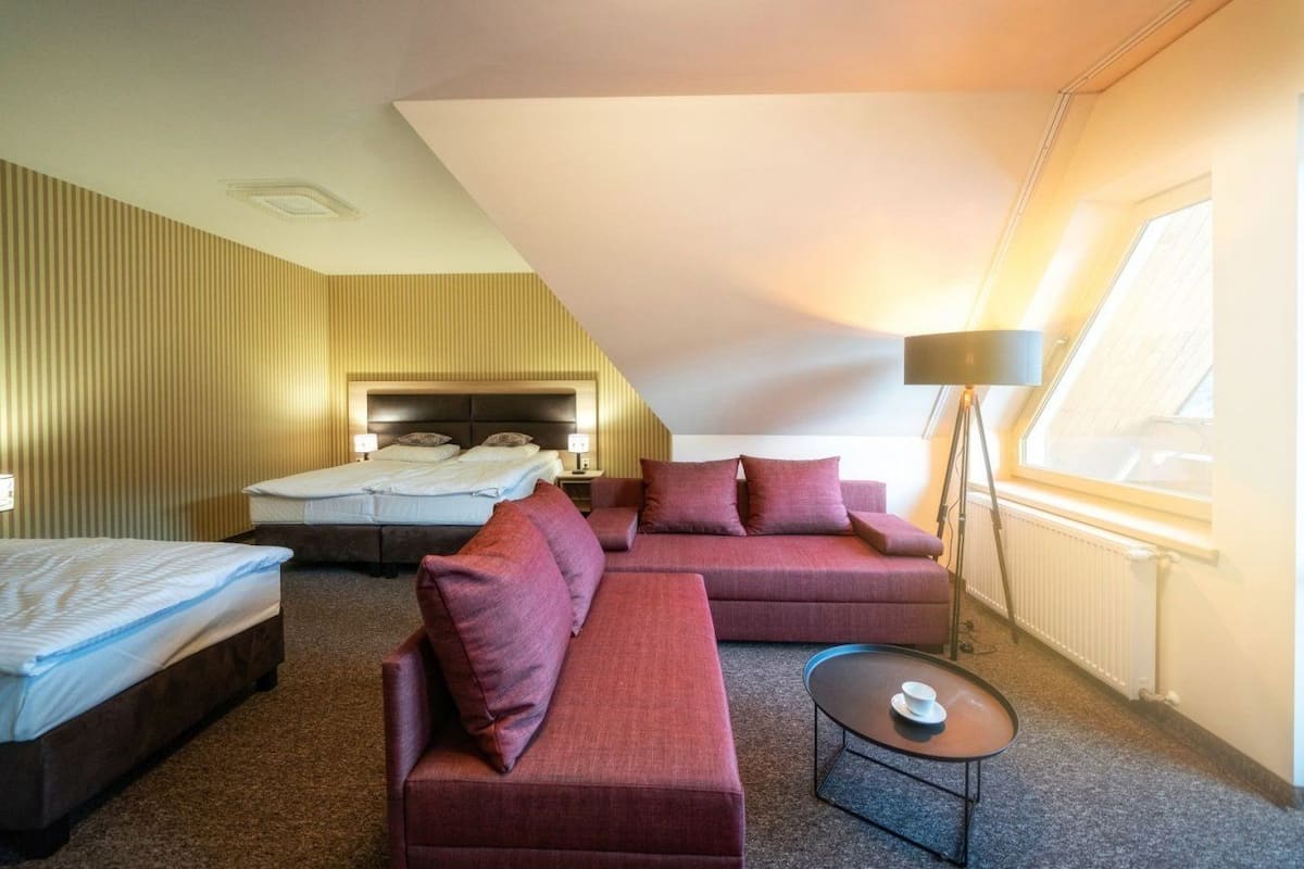 Een hotelkamer met een schuine plafond, een bed, een bank, een kleine tafel en een lamp.