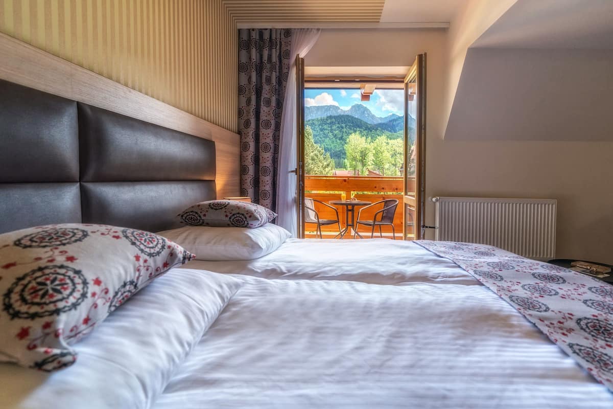 Een slaapkamer met een groot bed, uitzicht op bergen door een open deur, en een kleine tafel en stoel buiten.