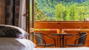 Une chambre avec un lit, une fenêtre donnant sur les montagnes, une table avec des chaises et un verre de jus d’orange.
