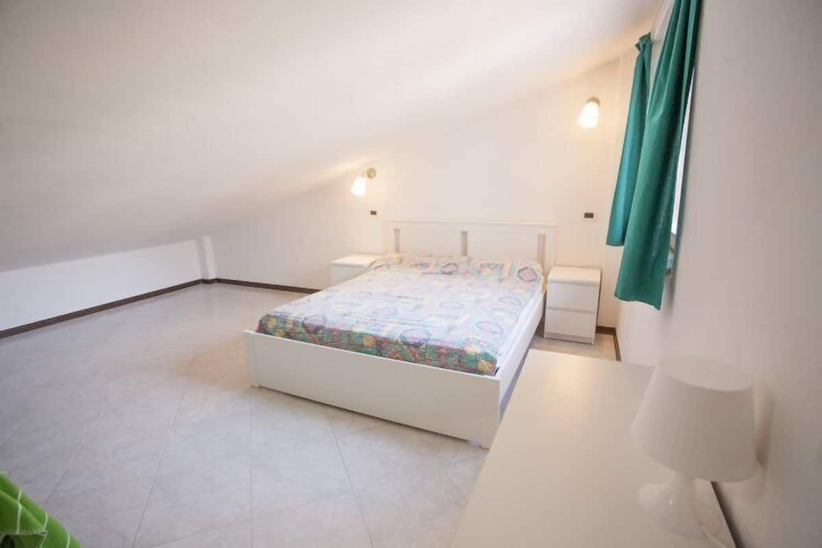 A bedroom with a bed, bedside tables, a lamp, and a window with curtains.