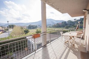 Un balcon avec vue sur les montagnes et les champs, une table, des chaises et une balustrade.
