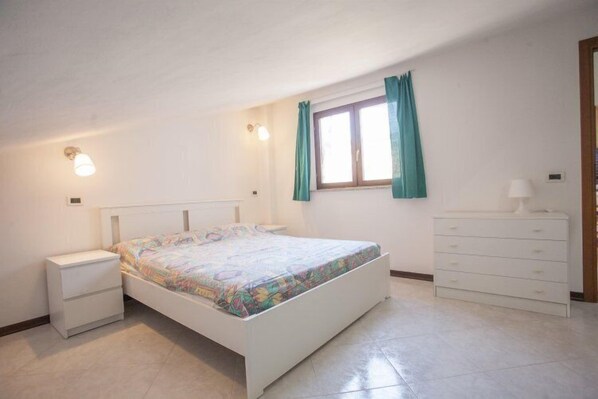Une chambre à coucher avec un lit, une table de chevet, une commode et une fenêtre avec des rideaux.