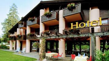 Un hotel con un área de estar al aire libre techada, varios balcones con jardineras y una vista despejada del paisaje circundante.