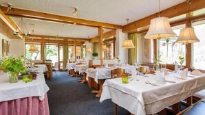A restaurant with multiple tables set for dining, wooden beams on the ceiling, and large windows allowing natural light. - T3 Hotel Mira Val (Flims)