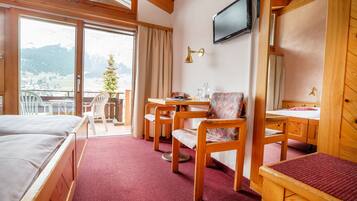 Une chambre d’hôtel avec un lit, un bureau, une chaise, une télévision et une vue sur les montagnes.
