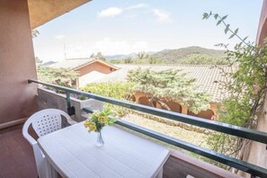 A balcony with a white table and chair, a vase with flowers, and a view of a building and trees. - Residence Acquabona (Portoferraio)