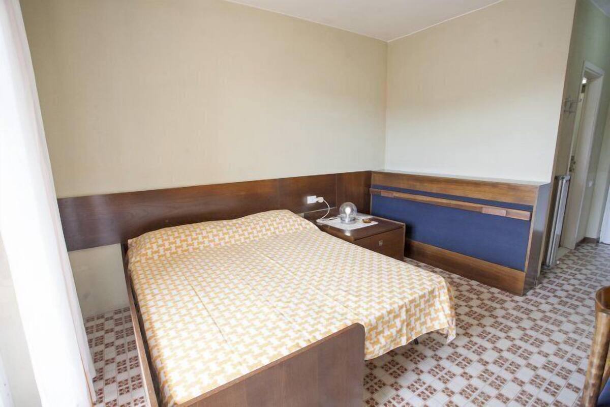 Um quarto pequeno e simples com uma cama, uma mesinha de cabeceira e uma escrivaninha.
