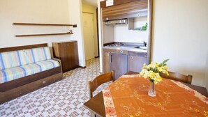 En kompakt opholdsstue med en sofa, et spisebord med blomster og et tekøkken.