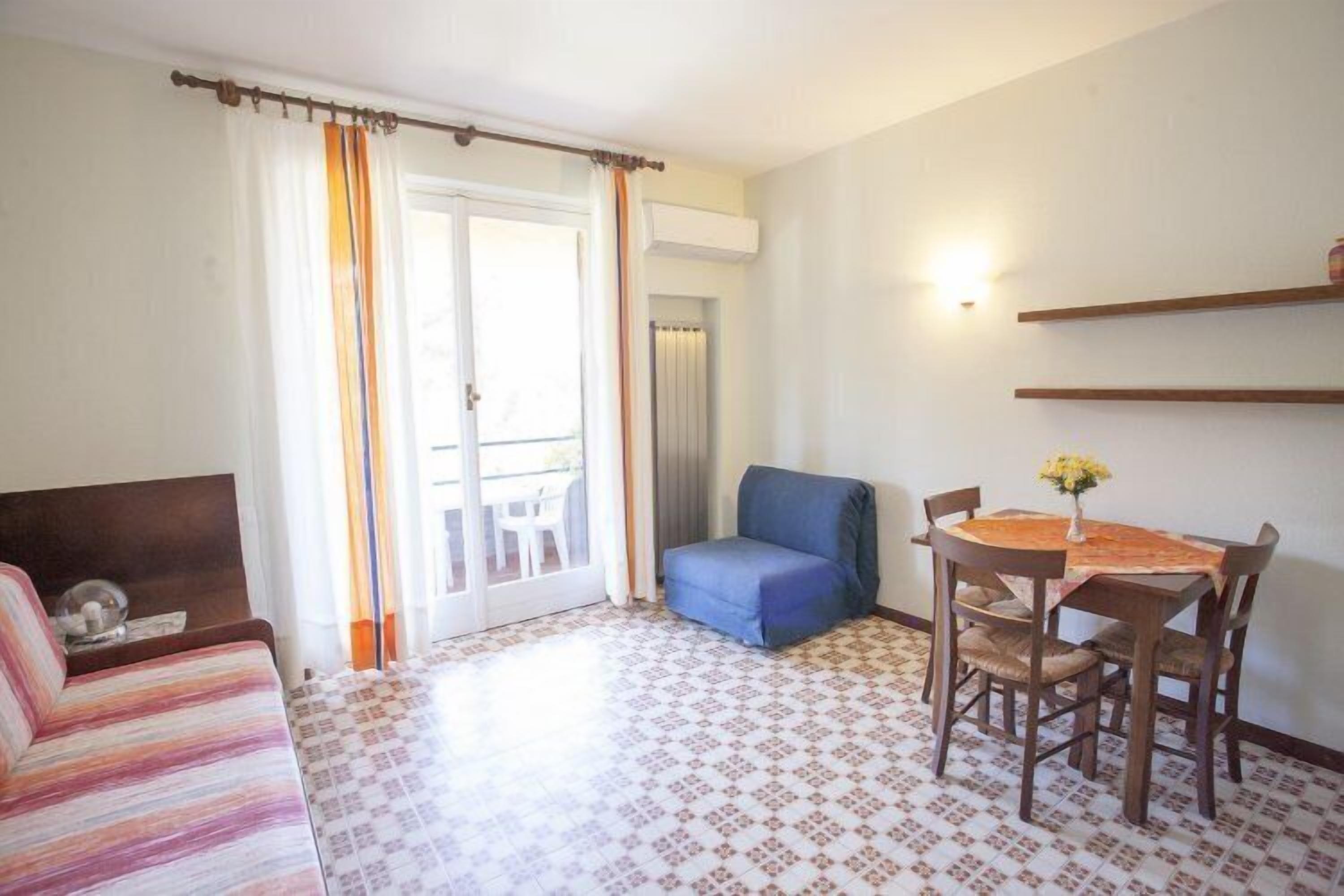 A room with a patterned floor, a sofa, a dining table with chairs, a blue chair, and a small table with a vase.