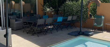 A poolside area with a covered seating area, lounge chairs, and a swimming pool.