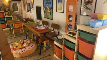 A child's playroom with a wooden table, chairs, storage bins, and educational posters on the walls.