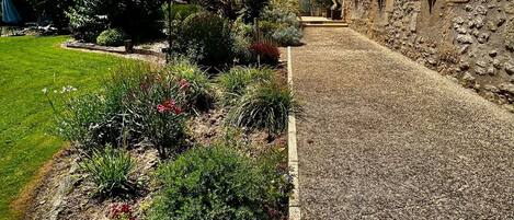 A stone building with a gravel pathway and a garden with various plants and a blue umbrella.