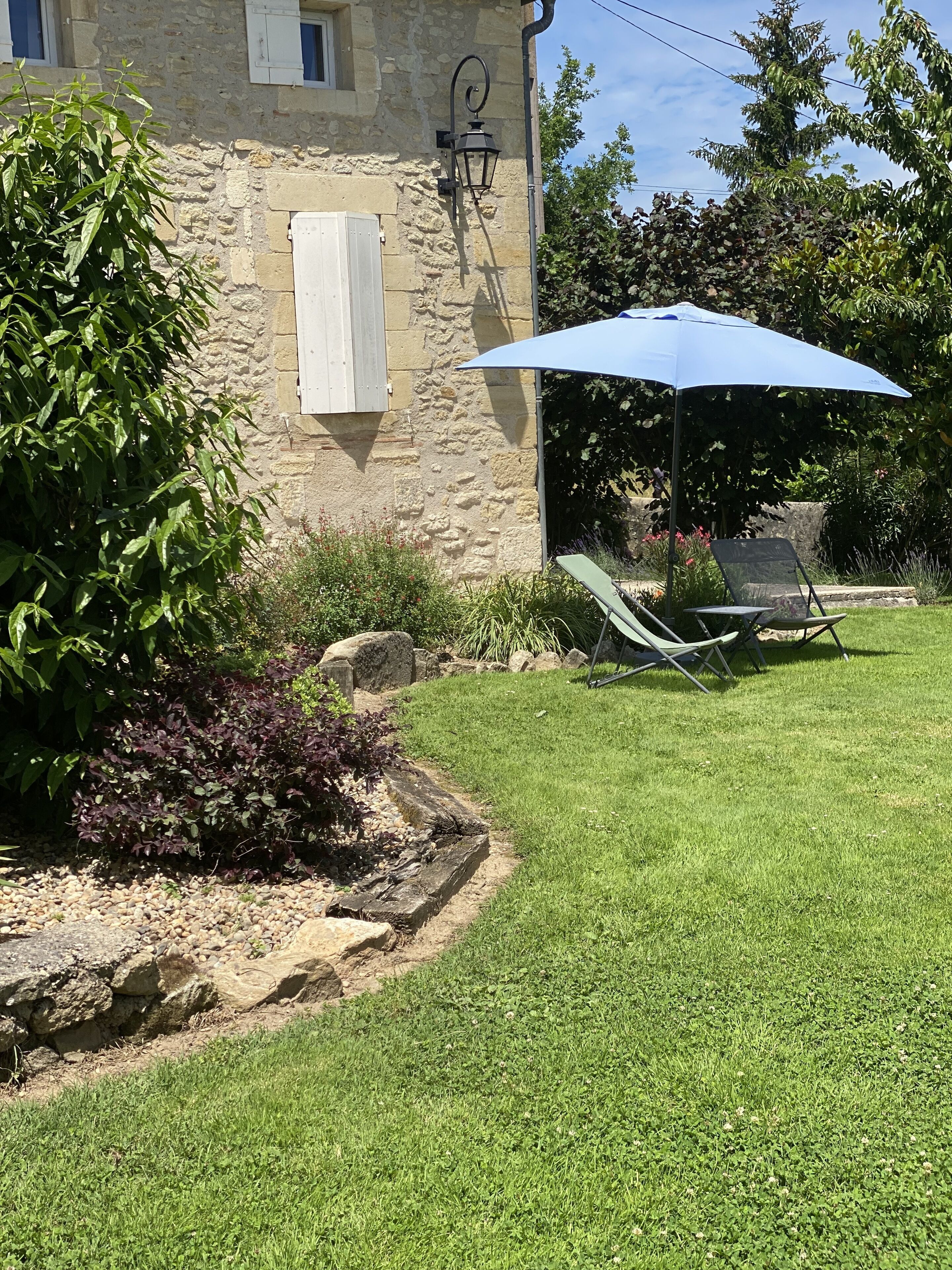 Un bâtiment en pierre doté d’un jardin comprenant une pelouse, un parasol bleu et des sièges d’extérieur.