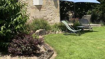Un bâtiment en pierre doté d’un jardin comprenant une pelouse, un parasol bleu et des sièges d’extérieur.