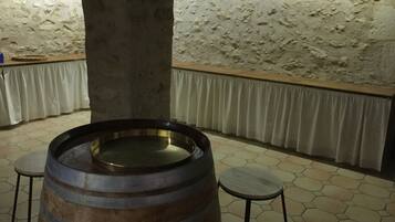 A rustic interior with a large wooden barrel, two stools, a stone wall, and a white curtain.