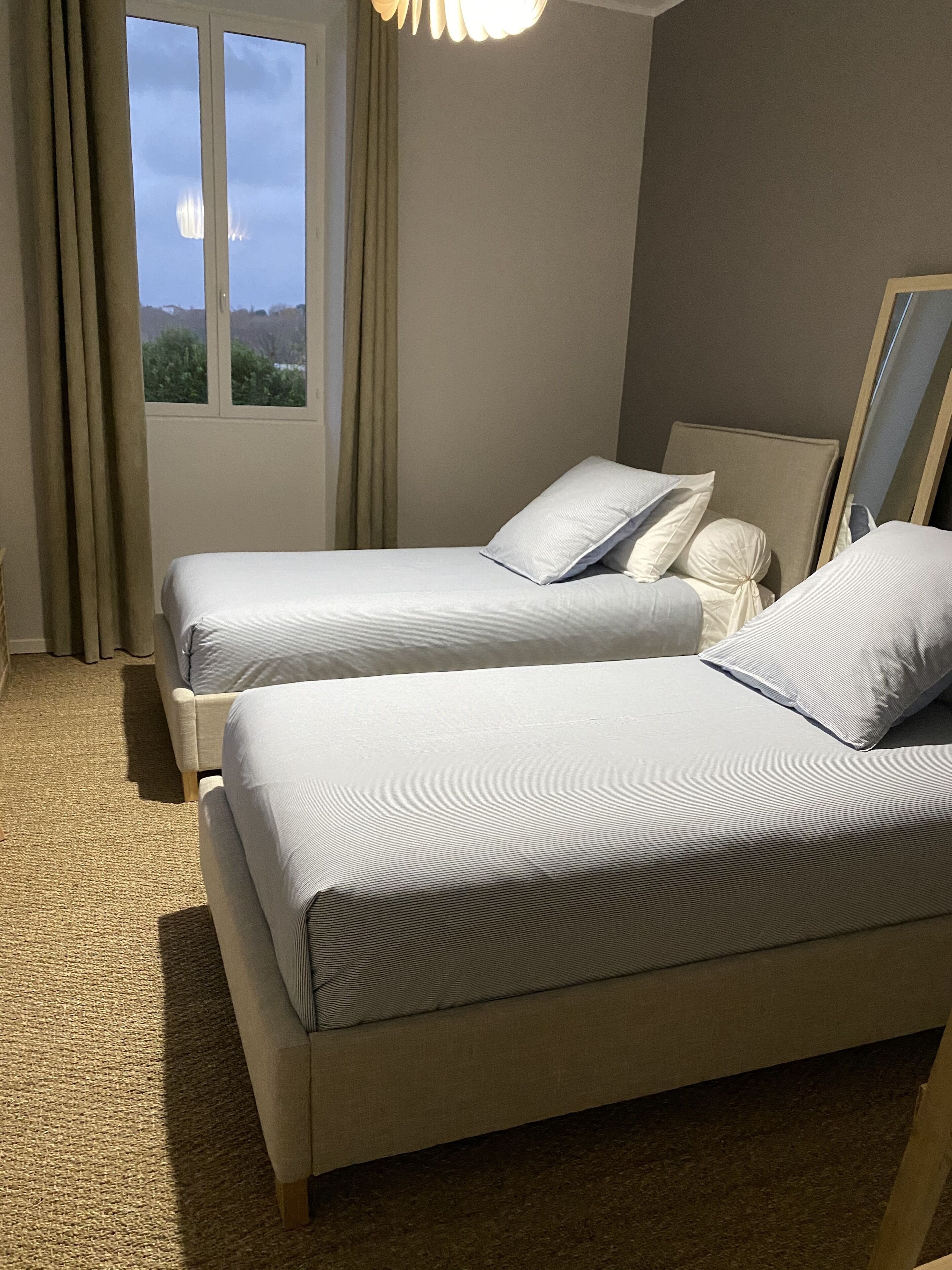 Habitación de hotel con dos camas, una ventana con cortinas, piso alfombrado y un espejo en la pared.