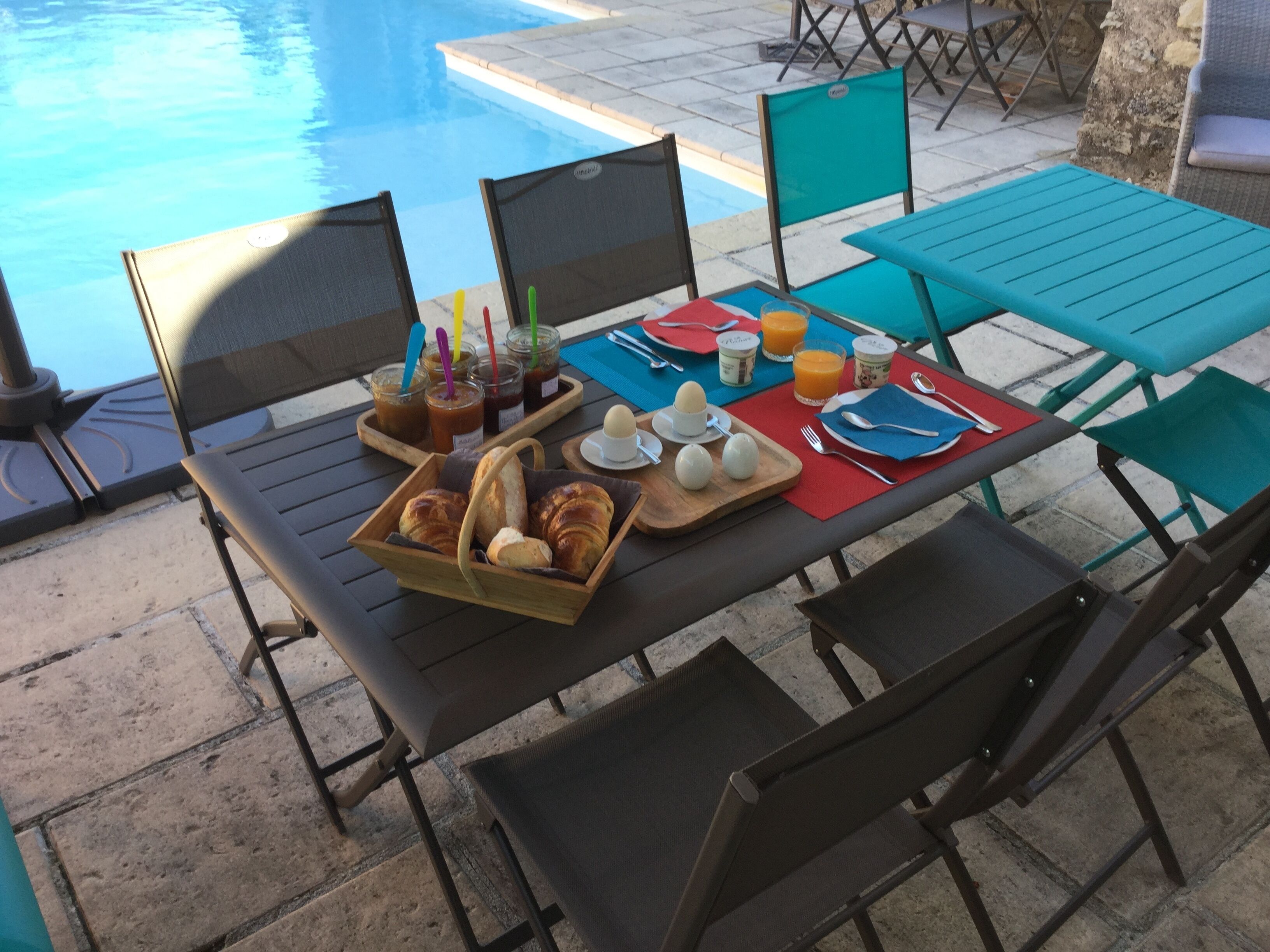 A poolside breakfast setup with chairs, a table, and food items.