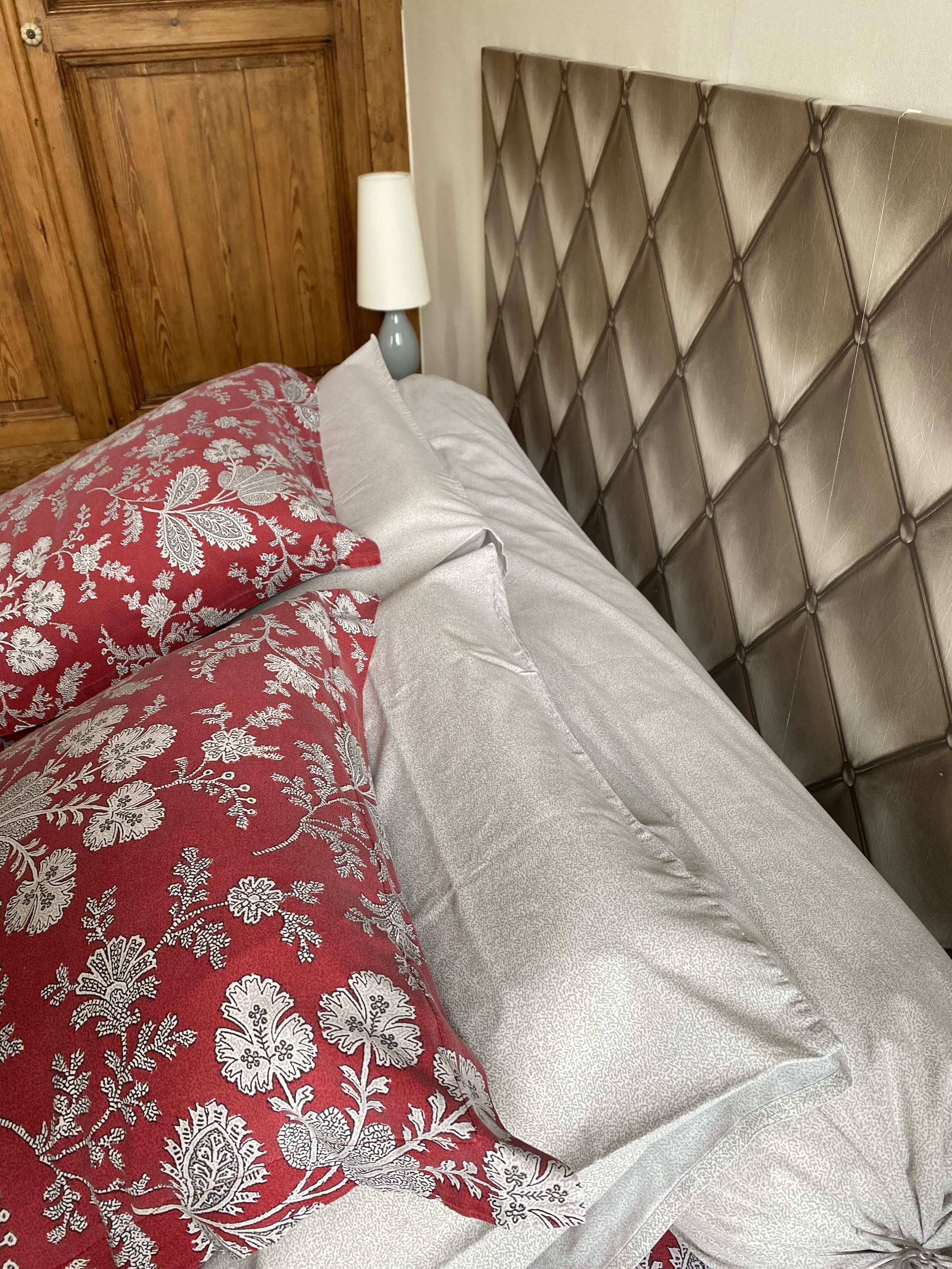 A bed with a tufted headboard, a wooden door, and a bedside lamp.
