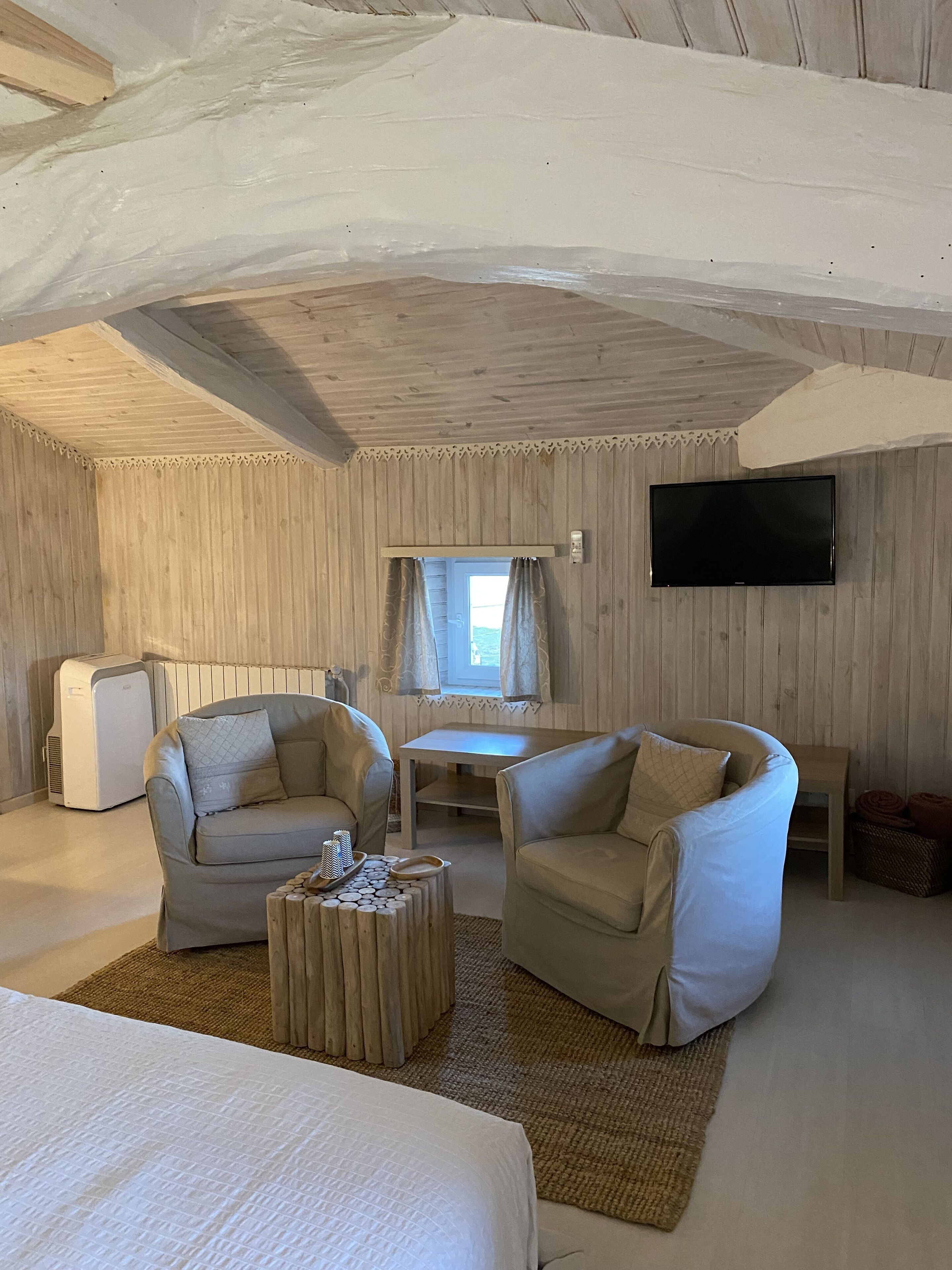 Una habitación acogedora con una cama, dos sofás, una mesita y un televisor montado en la pared.
