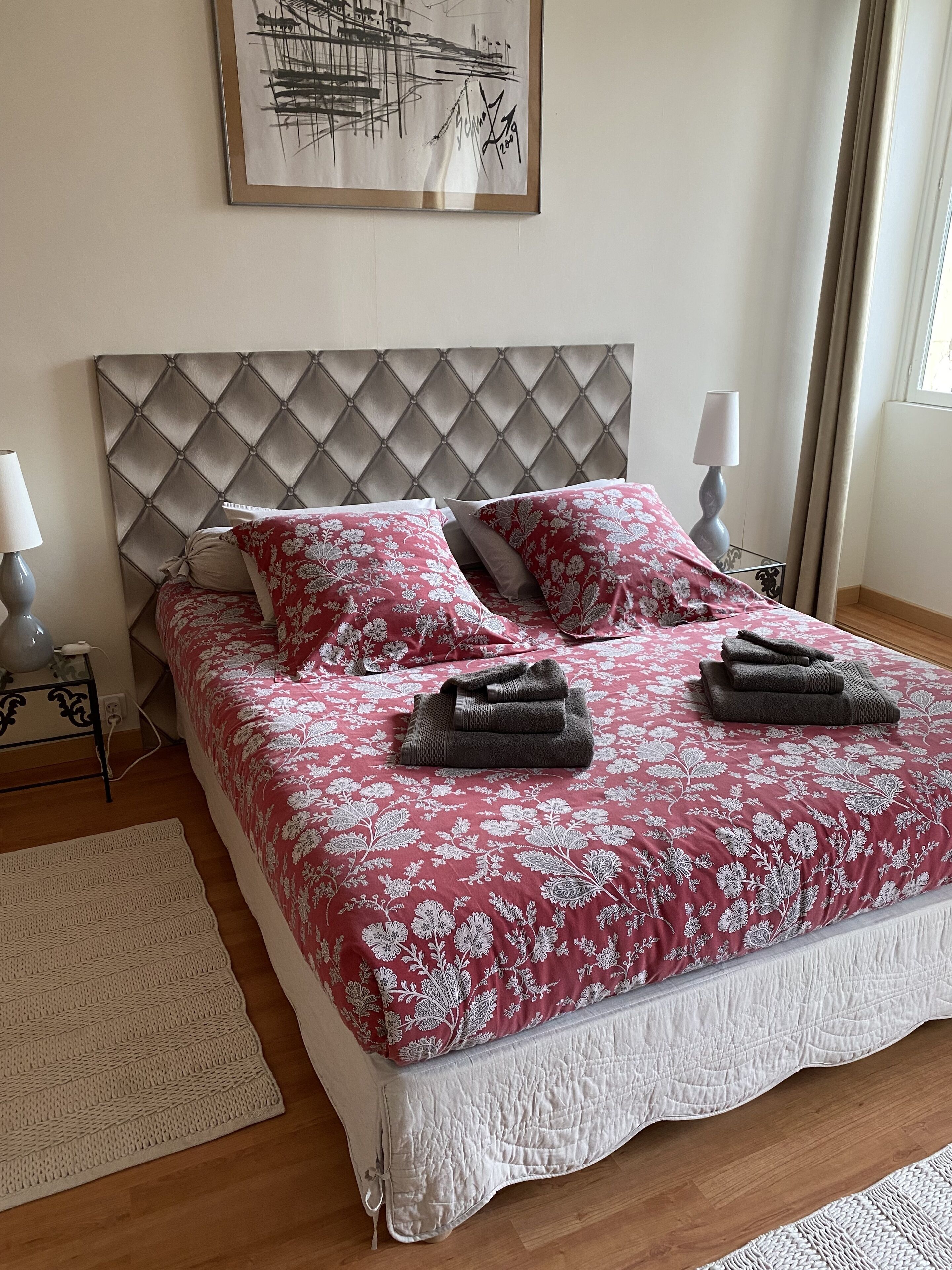 Ein ordentlich gemachtes Bett mit einer blumigen Tagesdecke, zwei Kissen und gefalteten Handtüchern.