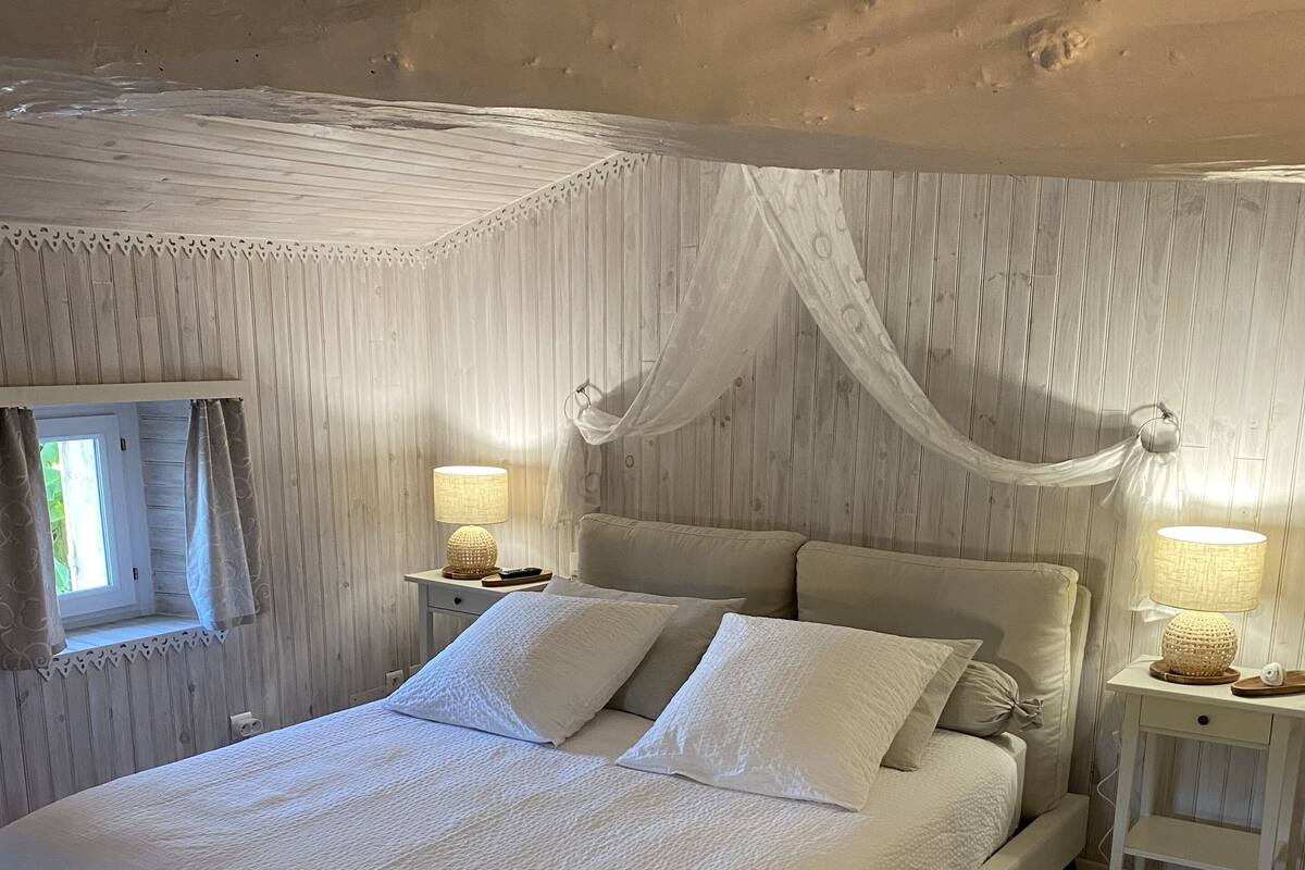 Een ruime slaapkamer met een groot bed, twee nachtkastjes met lampen, een raam met gordijnen en een kamerbreed tapijt met patroon.
