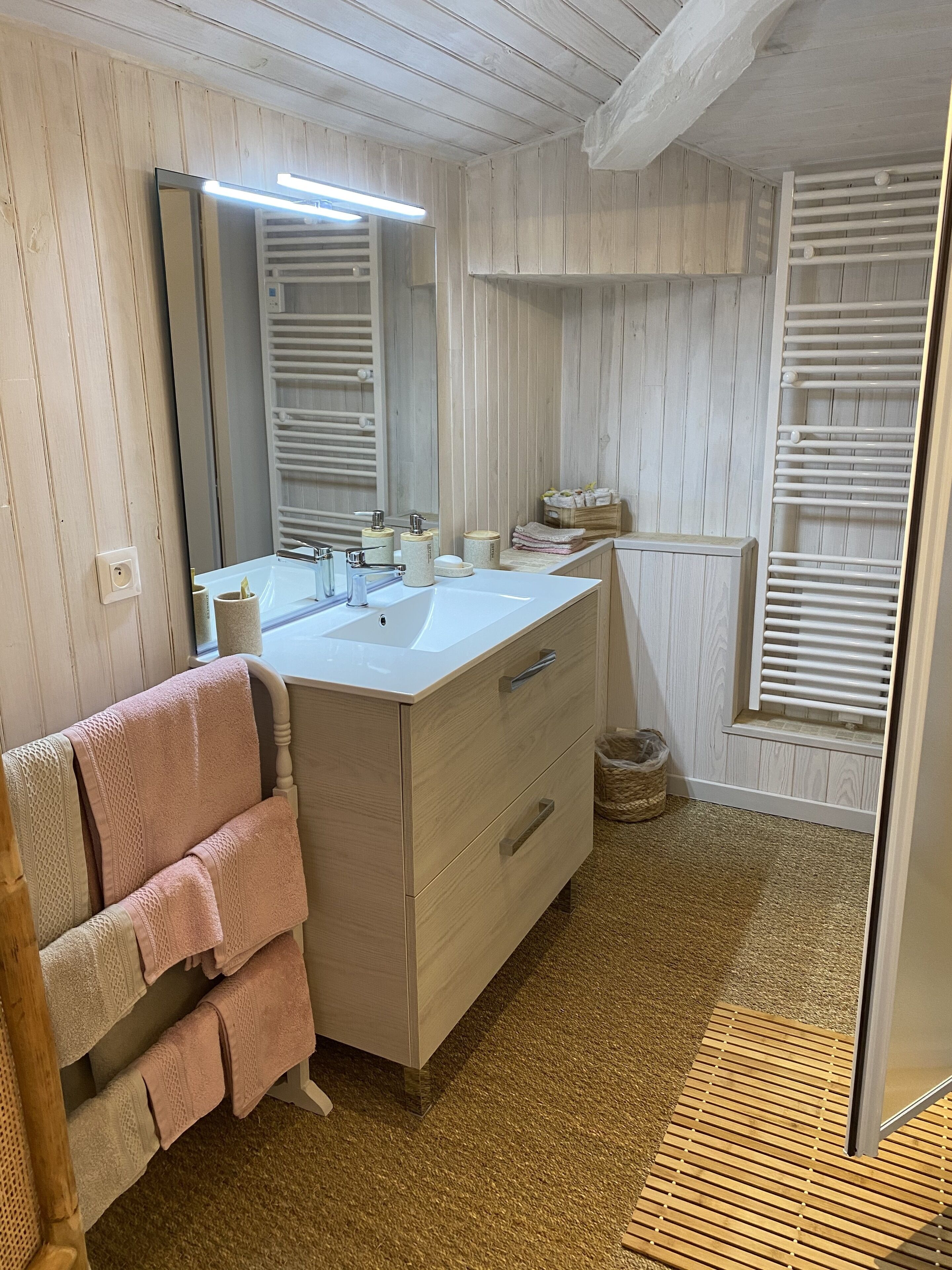 Een badkamer met een houten wastafelmeubel, een spiegel, een handdoekhouder en een douchehoek.