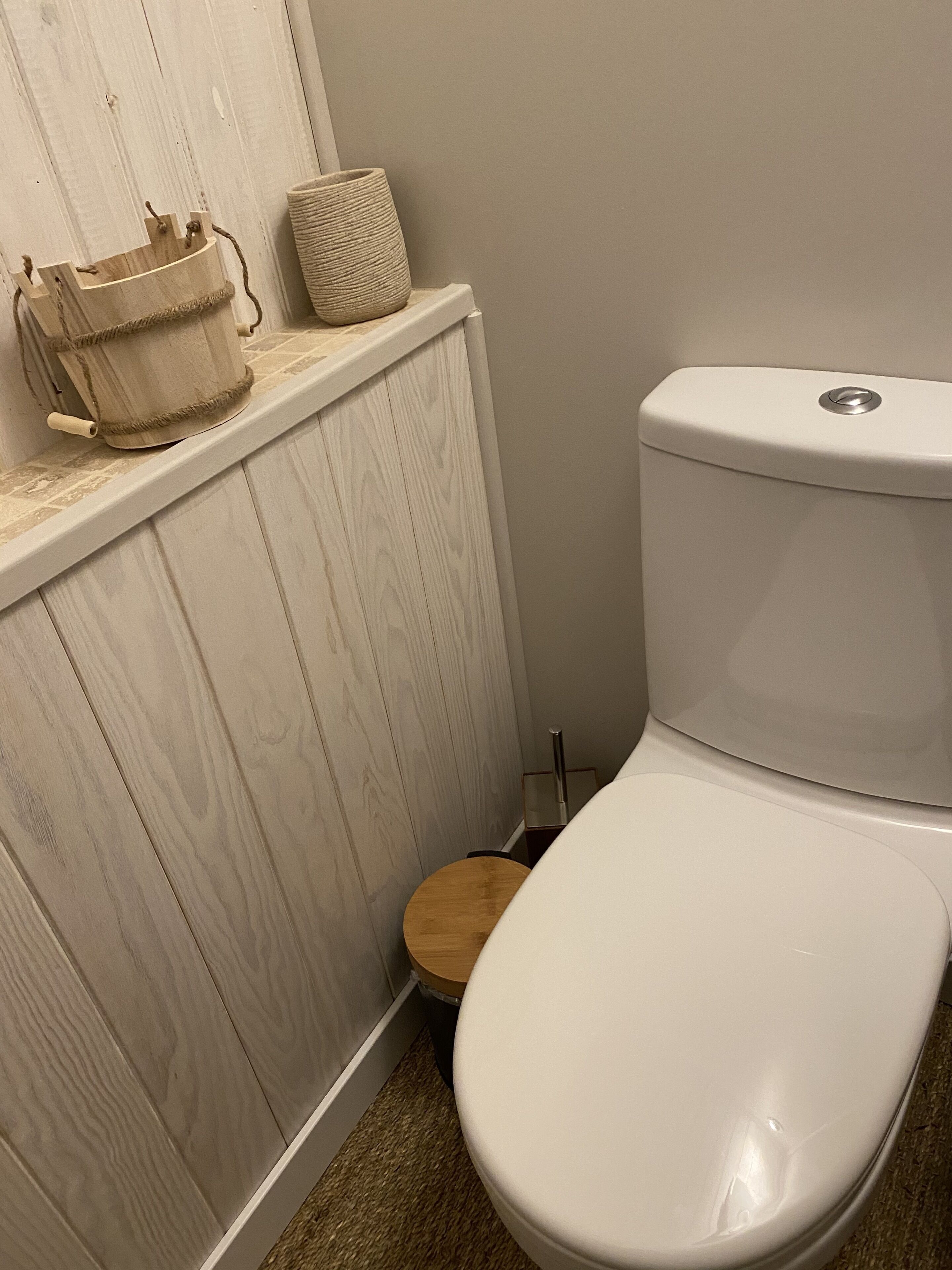 Un baño con inodoro blanco, tocador de madera y un taburete pequeño de madera.