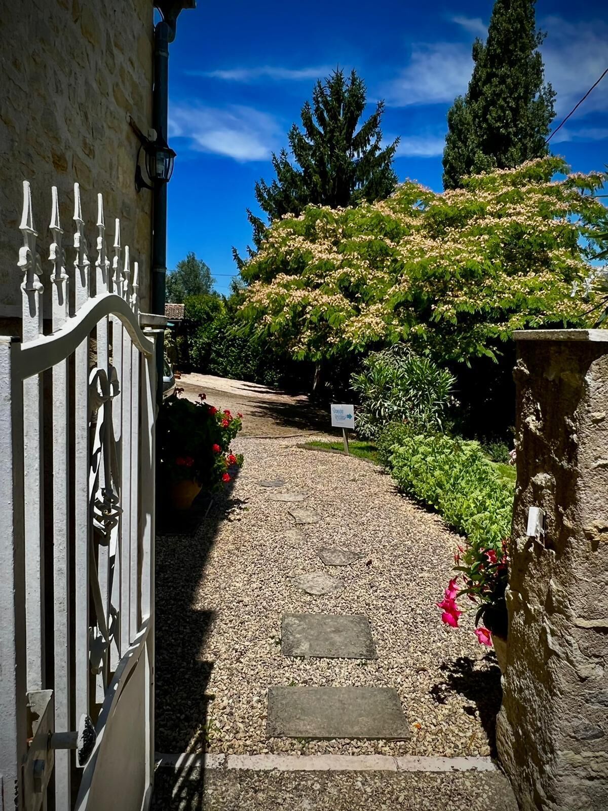 Un sendero de grava que conduce a una entrada con puerta, un muro de piedra y un cartel.