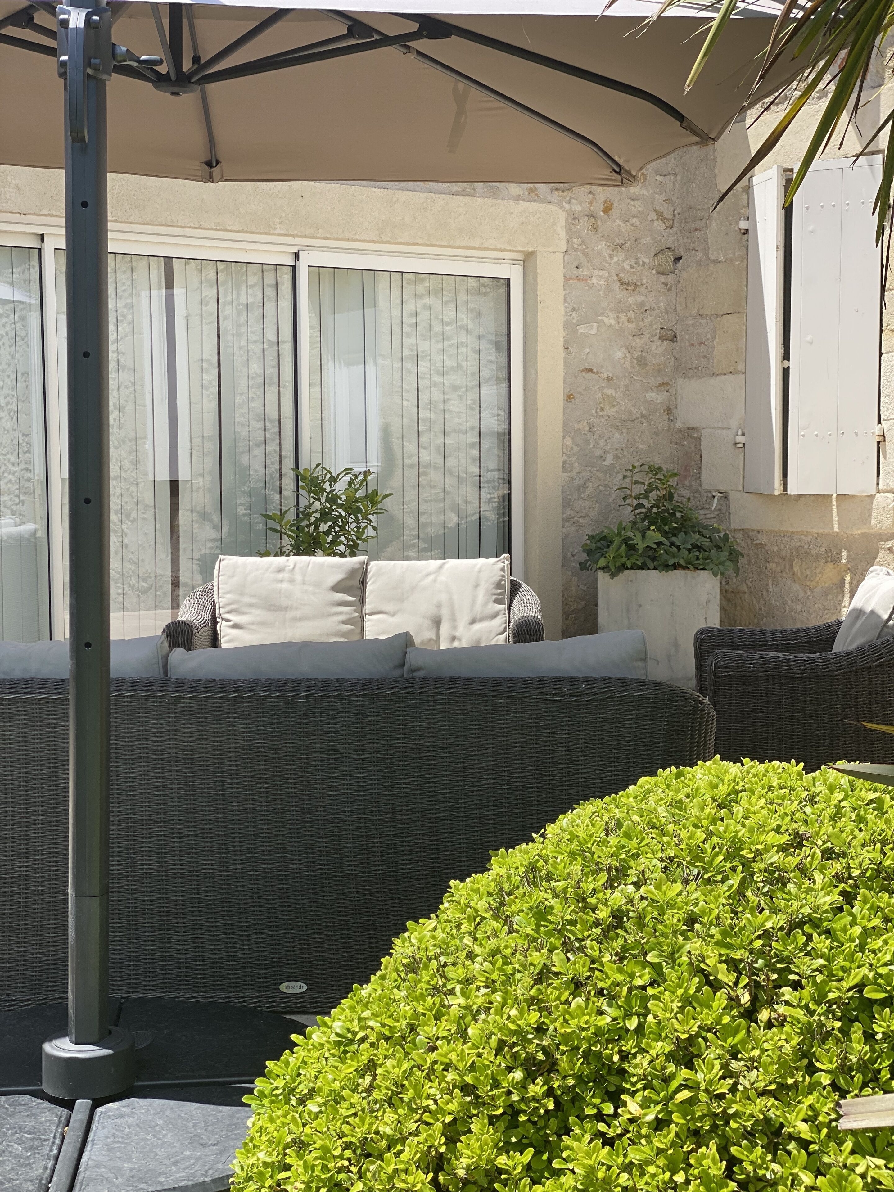 Un espace de détente extérieur aménagé avec des meubles en osier, des coussins, une plante en pot et un mur en pierre.