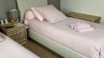 Habitación doble con dos camas, cada una con cabecero y piecero a juego, una mesita de noche con lámpara y una pequeña mesita auxiliar de madera.