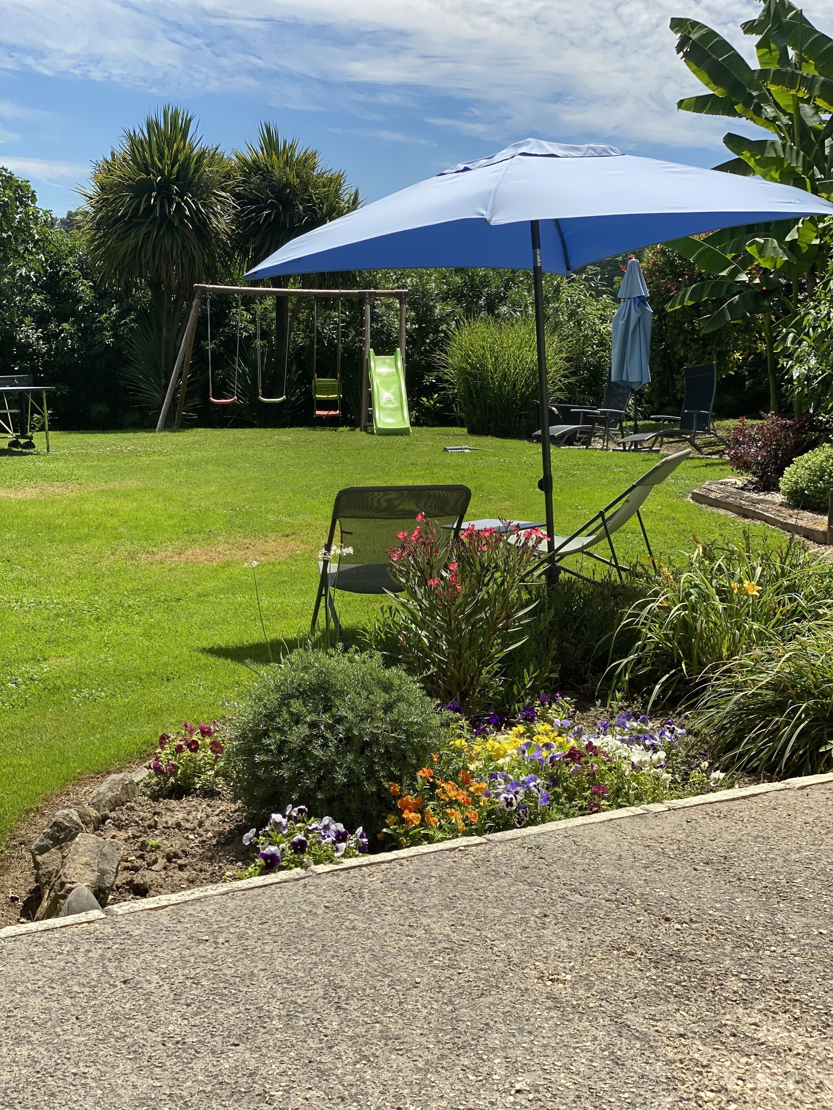 A backyard with a swing set, a slide, and a seating area under a blue umbrella.