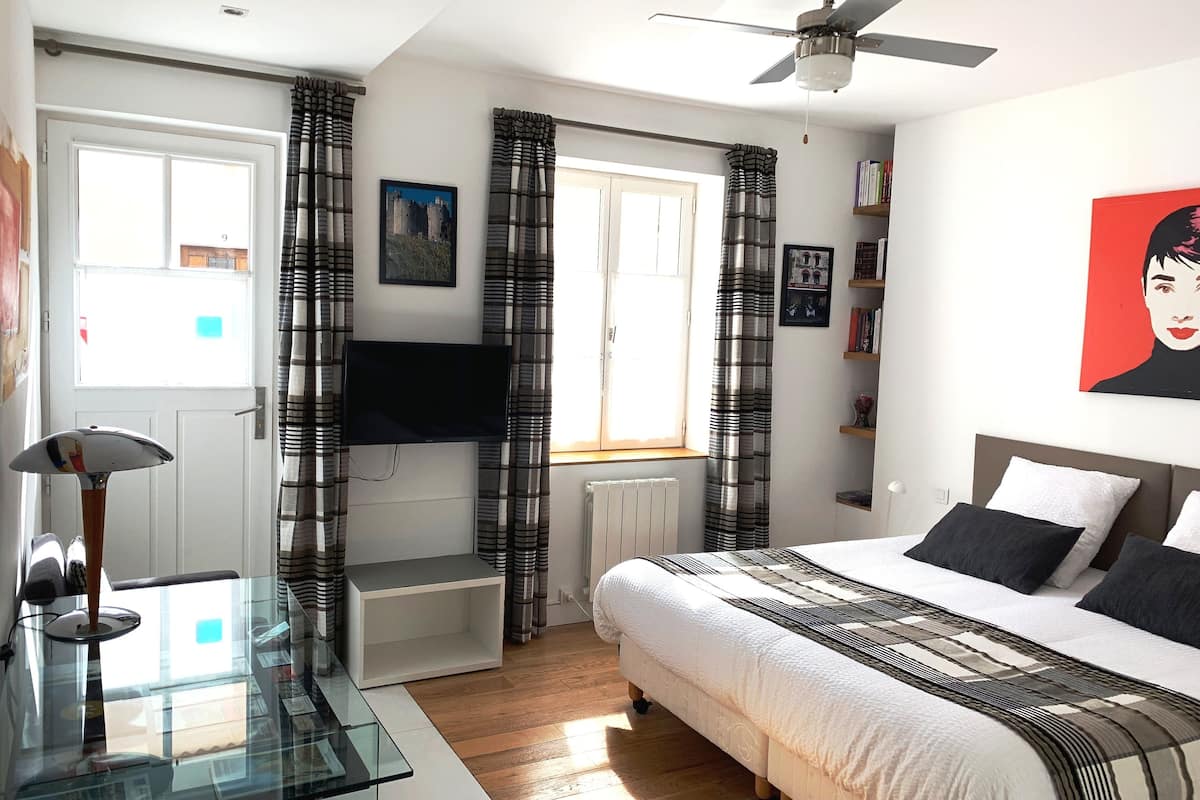 Een slaapkamer met een bed, een plafondventilator, een televisie, een glazen tafel en gordijnen.