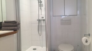 Een badkamer met een douche met glazen wand, een toilet en een wastafel met handdoekhouder.