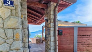 A stone building with a wooden roof, a red door, and a view of the sea. - Villa Vosilla (Opatija)