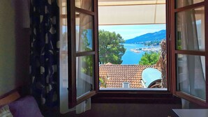 A room with a large window offering a view of a coastal landscape, including a body of water and distant mountains. - Villa Vosilla (Opatija)