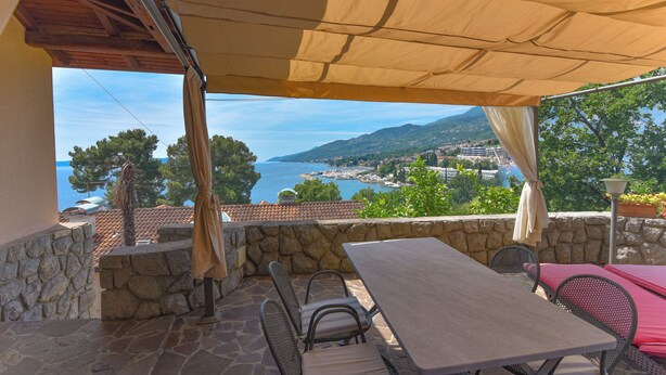 A patio with a table and chairs, a stone wall, and a view of the sea and mountains. - Villa Vosilla (Opatija)