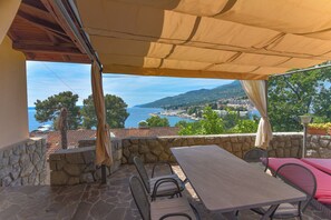 A patio with a table and chairs, a stone wall, and a view of the sea and mountains. - Villa Vosilla (Opatija)