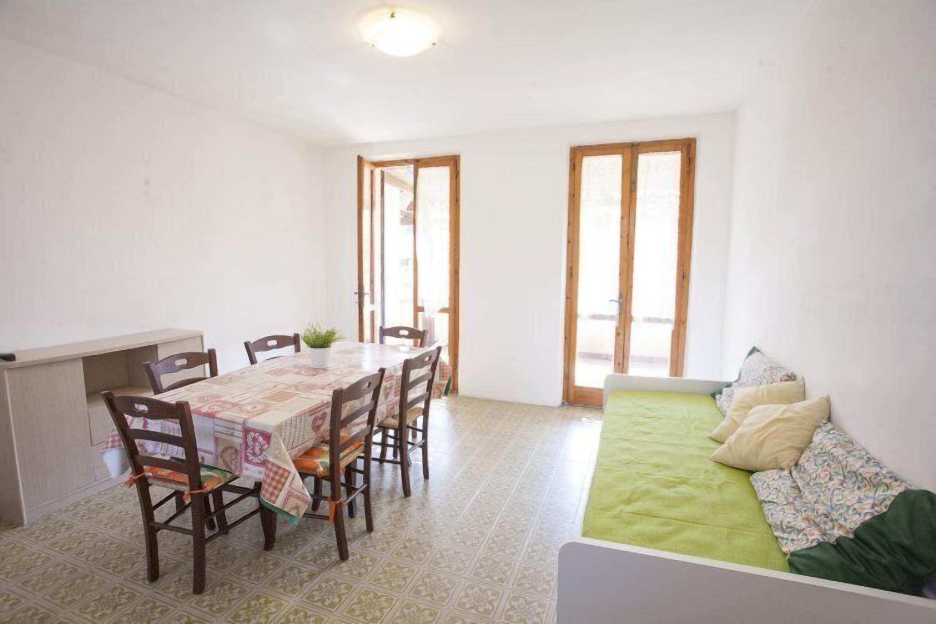 A room with a dining table set for four, a sofa, and a small kitchen area.