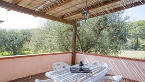 A covered outdoor patio with a table and chairs, a lantern, and a view of olive trees. - Appartamenti Le Mimose (Capoliveri)