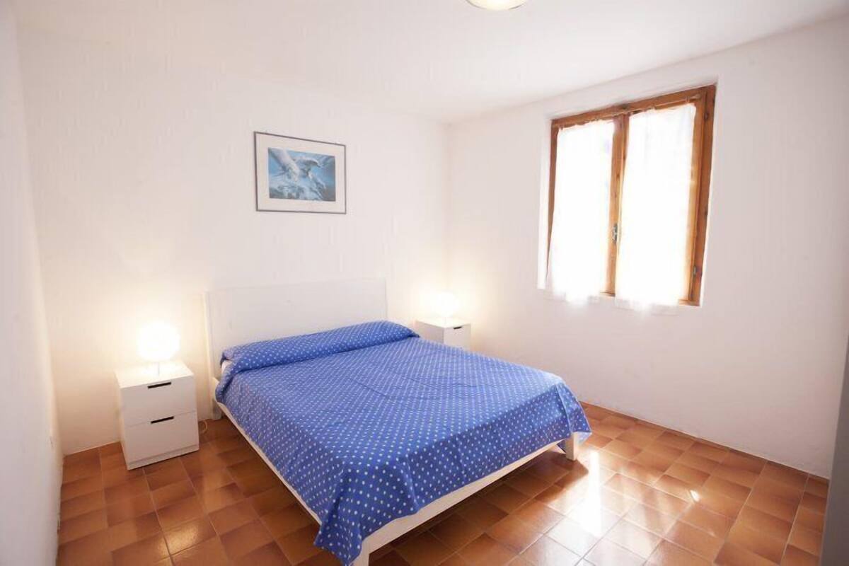 A bedroom with a bed, two bedside tables, a nightstand, a window, and a framed picture on the wall.
