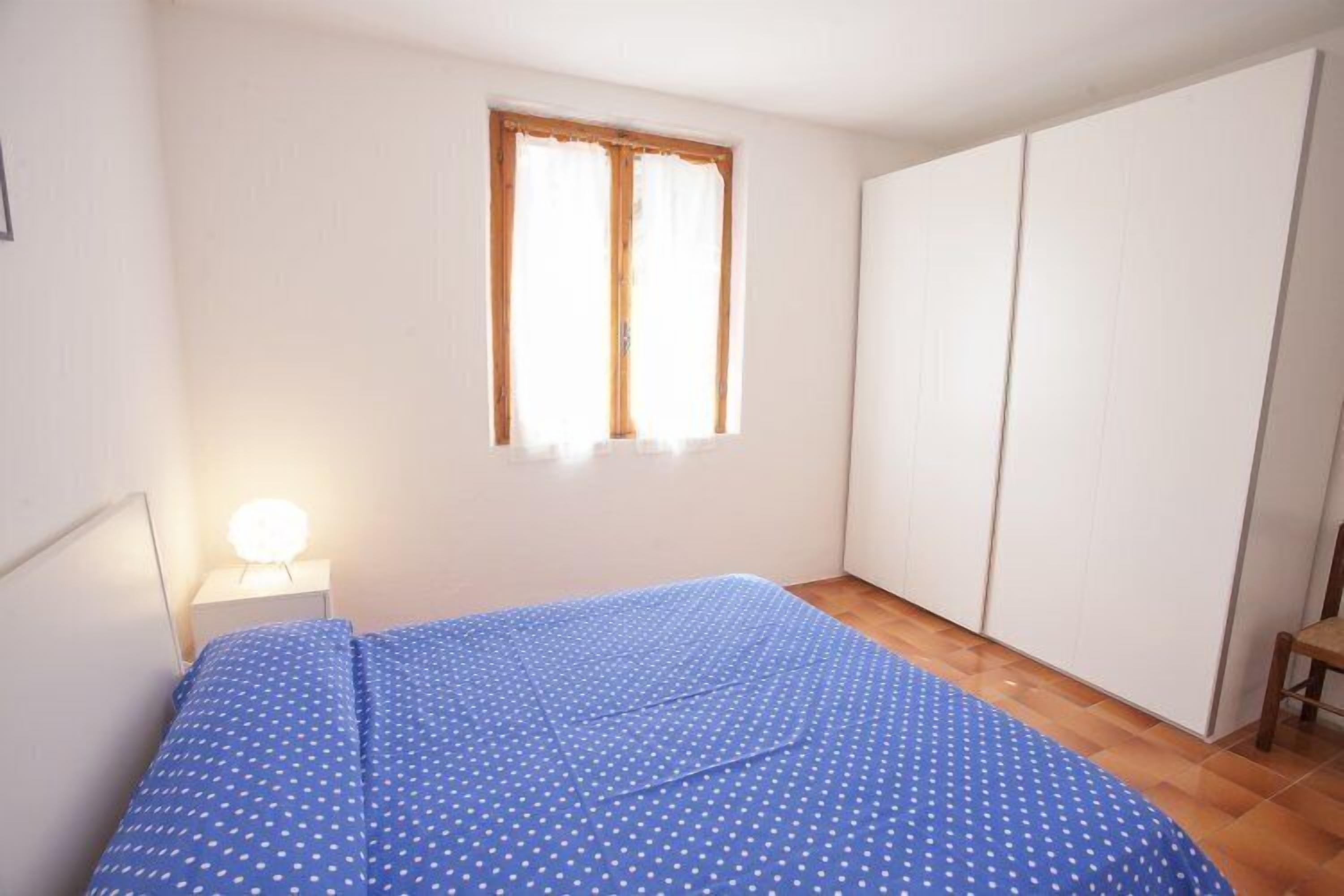 Un dormitorio con cama, mesita de noche, ventana y armario.
