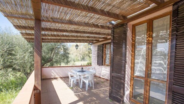 A covered patio with a table and chairs, large windows with decorative glass, and a view of greenery. - Appartamenti Le Mimose (Capoliveri)