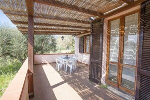 A covered patio with a table and chairs, large windows with decorative glass, and a view of greenery. - Appartamenti Le Mimose (Capoliveri)