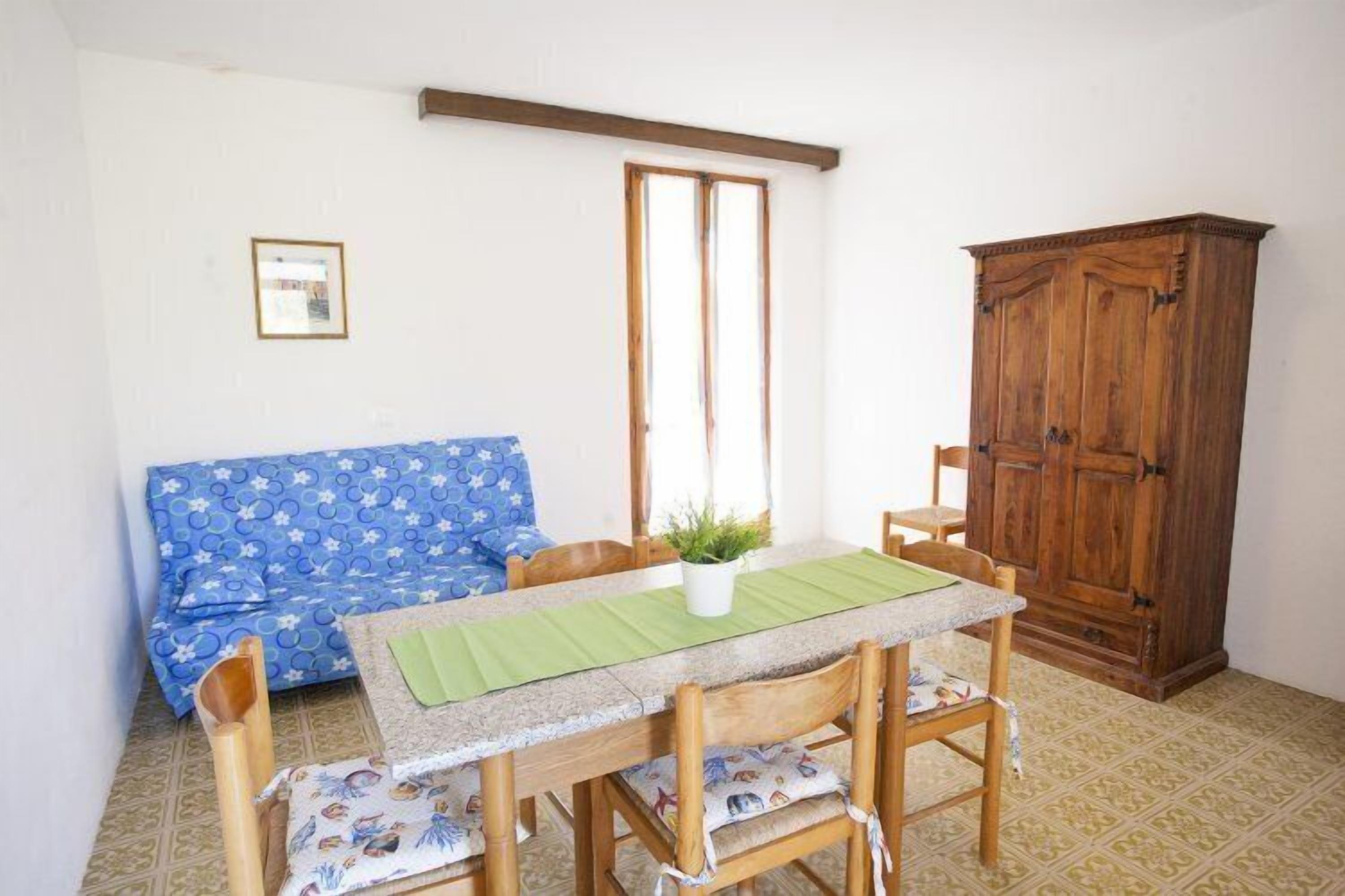 A room with a dining table, chairs, a blue patterned sofa, a wooden cabinet, and a window.