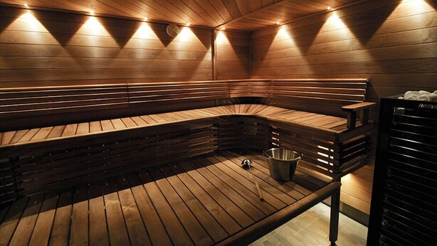 A sauna with wooden benches and a metal bucket on the floor. - Hotelli Toivola (Kemi)