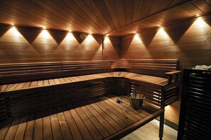A sauna with wooden benches and a metal bucket on the floor. - Hotelli Toivola (Kemi)